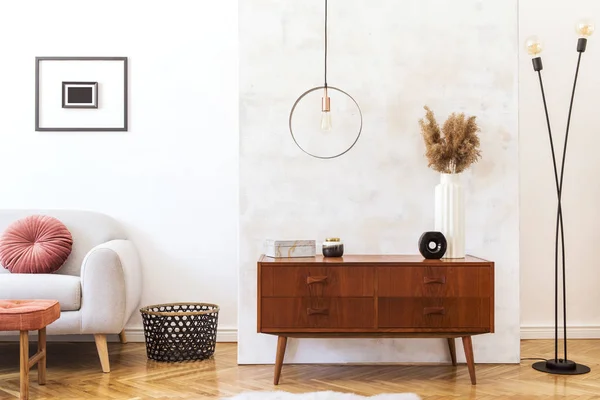 Stylish and retro interior of living room with design commode, gray sofa, round pendant lamp, vintage footrest, elegant accessories and mock up photo frames. Minimalistic home decor of sitting room.