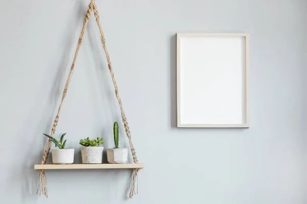 Stylish and minimalistic scandinavian interior with mock up poster frame and hanging wooden shelf with beautiful cacti in cement pots. Modern home decor. Template. Gray background walls. Home garden.