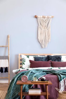 Tasarım mobilyalar, bej macrame, zarif aksesuarlar ve kitaplar ile gece masası ile yatak odası şık ve lüks iç. Güzel çarşaflar, battaniyeler ve yastıklar. Rahat ev dekorasyonu. Gri duvarlar.