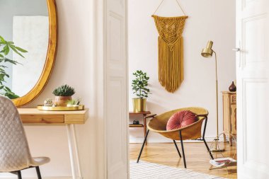 Altın koltuk, ahşap ayna, tasarım mobilya ve aksesuarları, bitkiler, lamba ve beyaz duvarda büyük makrame ile daire stüdyo şık ve sıcak iç. Oturma odası modern ev dekorasyonu. 