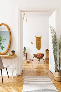 Büyük ayna, tuvalet masası, altın koltuk, tasarım aksesuarları ve mobilya, bitkiler, palmiye yaprakları, sarı makrame ile daire Güneşli scanidnavian iç. Odaların şık ev dekorasyonu. 