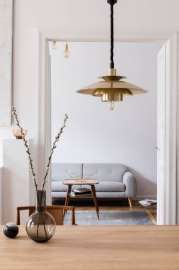 Şık ve modern scandi iç tasarım ahşap masa, sandalye, kanepe ve asılı altın lamba ile. Tasarım mobilya ve aksesuarları ile minimalist alan. Beyaz duvarlar. Gerçek fotoğraf. 