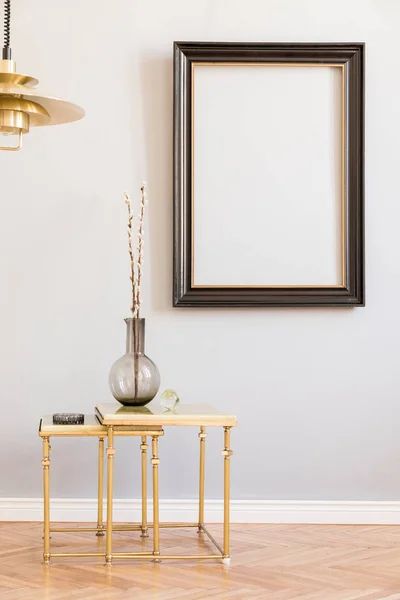 Stylish and design retro interior with design gold lamp and small table with vase. Black mock up frame on the grey background wall. Minimalistic concept of sitting room. Real photo.