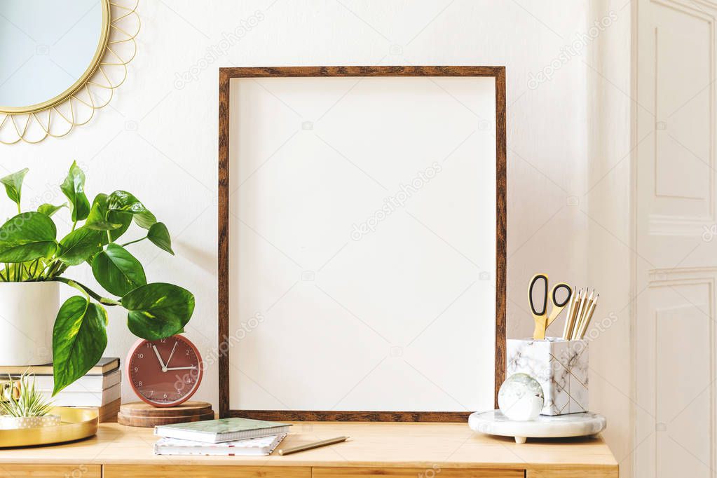 Modern scanidnavian interior with mock up photo frame, design office accessories and plants on the wooden desk. Beautiful mirror on the white wall. Creative desk of home decor. Warm and sunny room.