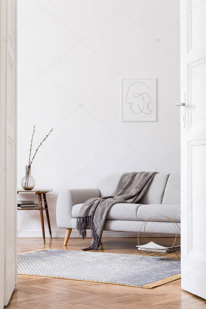 Stylish scandi interior of home space with design grey sofa and retro small table. Living room with design accessories and mock up poster frame. Elegant decor. Brown wooden parquet with modern carpet.