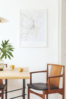 Poster haritası, masa tasarımı sandalyeler, altın pedant lamba ve kahve fincanpaylaşımı ile şık ve modern yemek odası iç. Beyaz duvarlar, ahşap parke. Vazodaki tropikal yapraklar. Eklektik dekor.