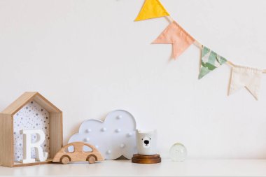 Beyaz duvar, kutu, oyuncak ayı fincan, oyuncaklar pamuk renkli bayraklar asılı şık ve modern İskandinav çocuk odası. ahşap aksesuarlar ve bulut. Gerçek fotoğraf. Kopya alanı. Rahat dekor.