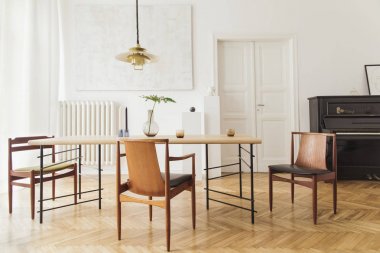 Eklektik ve zarif yemek odası iç tasarım paylaşım masası, sandalyeler, altın pedant lamba, soyut resimler, piyano ve şık aksesuarlar. Minimalist dekor. Kahverengi ahşap parke. Gerçek fotoğraf.