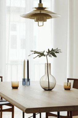Vazo, woonoden masa, mumlar ve altın lamba tropikal yaprak ile şık ve parlak iç. Tasarım aksesuarları ile modern oda. Eklektik ve minimalist ev dekorasyonu. Pencerelerde görünüm. Gerçek fotoğraf.
