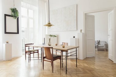 Eklektik ve zarif yemek odası iç tasarım paylaşım masası, sandalyeler, altın pedant lamba, soyut resimler ve şık aksesuarlar. Oturma odasına bak. Minimalist dekor. Kahverengi ahşap parke.