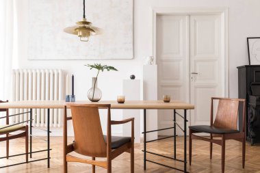 Eklektik ve zarif yemek odası iç tasarım paylaşım masası, sandalyeler, altın kolye lamba, soyut resimler, piyano ve şık aksesuarlar. Minimalist dekor. Kahverengi ahşap parke. Gerçek fotoğraf.