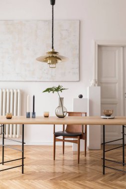 Eklektik ve zarif yemek odası iç tasarım paylaşım masası, sandalyeler, altın kolye lamba, soyut resimler ve şık aksesuarlar. Vazodaki tropikal yapraklar. Minimalist dekor. Gerçek fotoğraf.