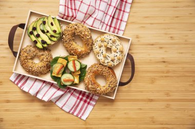 Kahverengi ahşap masada sebze, otlar, salça, tohum, humus ve marul ile salver vegan simit sandviç şık ve lezzetli kompozisyon. Taze ve sağlıklı kahvaltı. 