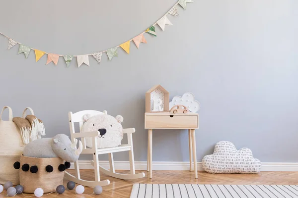 Scandinavian child room with grey wall, natural basket, teddy bear on children's chair and design toys. Cute modern interior with colorful cotton flags and wooden shelf with accessories. Copy space.