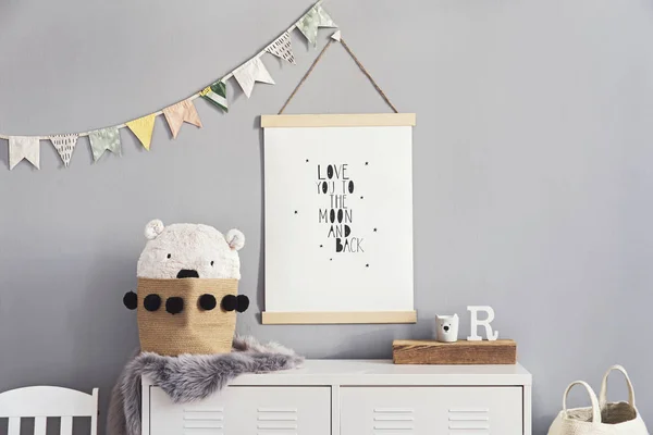 Stylish and cute scandinavian decor of kid room with mock up poster, white shelf, natural toys, hanging decor flags , child\'s armchair, basket for accessories and teddy bears. Minimalistic concept.