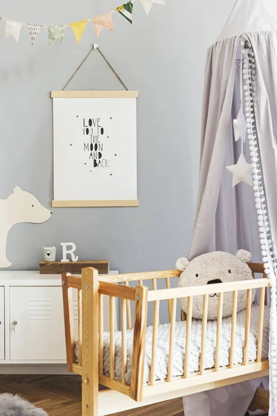 Stylish and cute scandinavian decor of newborn baby room with mock up poster , white design furnitures, natural toys, hanging grey canopy with wooden cradle, pillows, accessories and teddy bears.