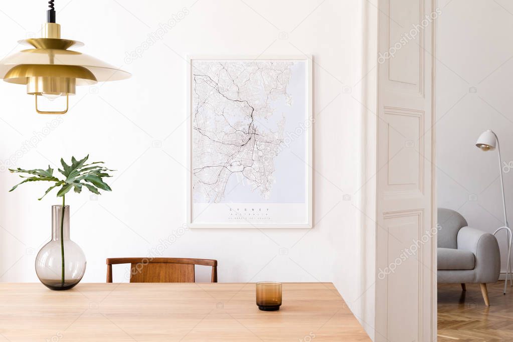 Stylish and eclectic dining room interior with mock up poster map, sharing table design chairs, gold pedant lamp and elegant sofa in second space. White walls, wooden parquet. Tropical leafs in vase.