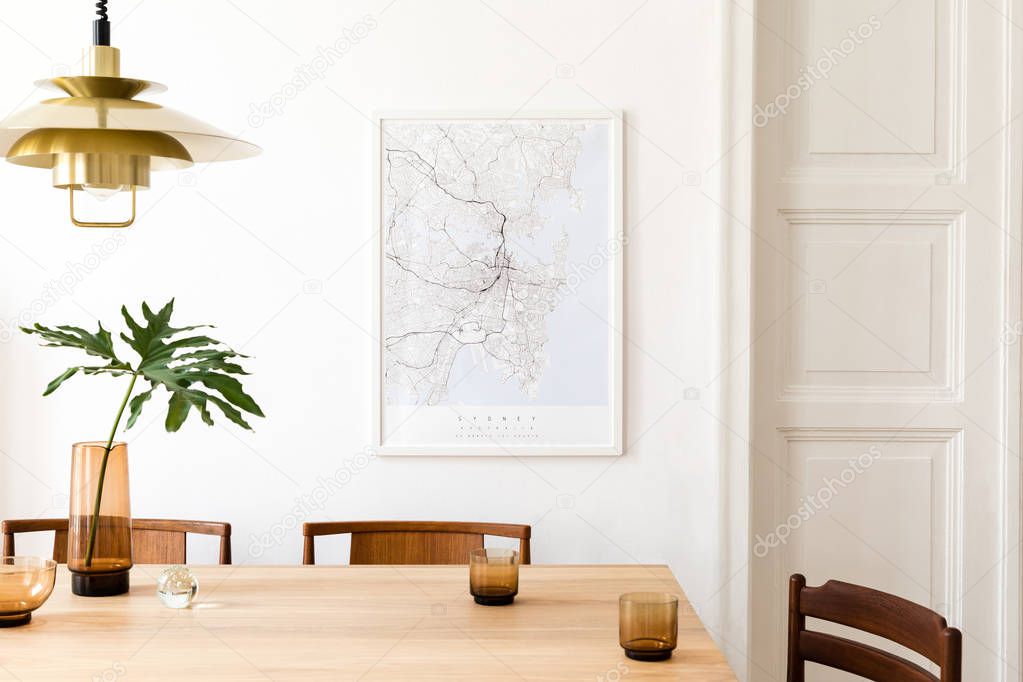 Stylish and modern dining room interior with mock up poster map, sharing table design chairs, gold pedant lamp and cups of coffee. White walls, wooden parquet. Tropical leafs in vase. Eclectic decor.