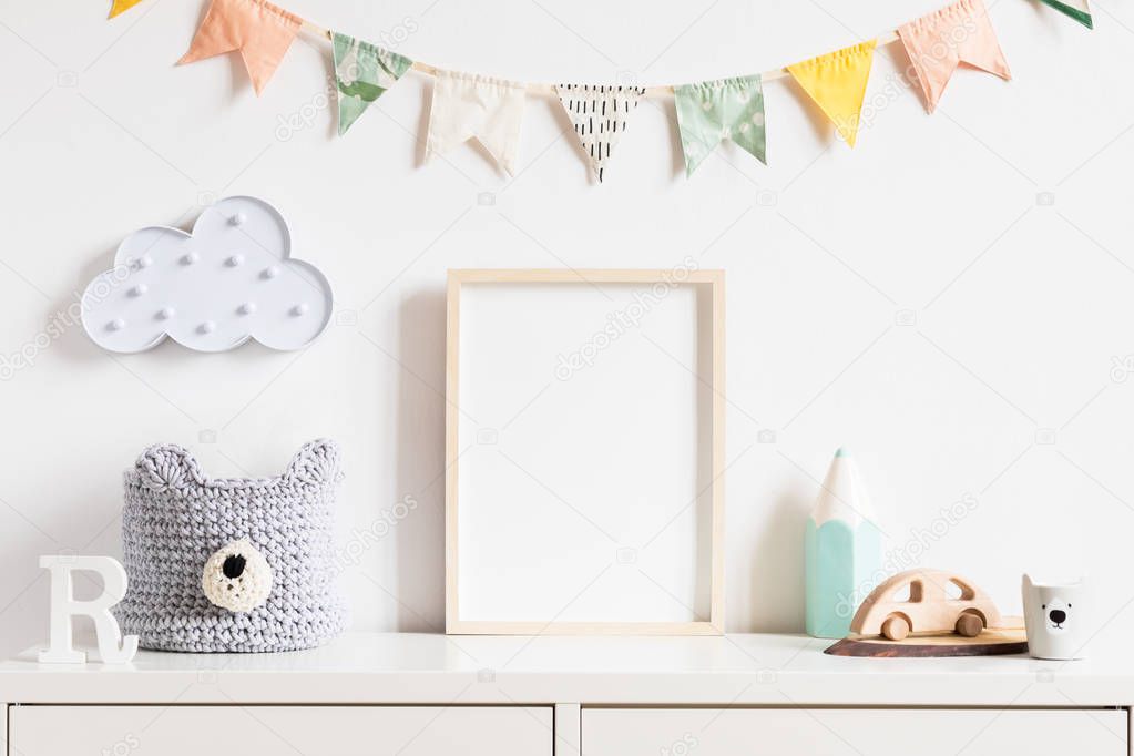 Stylish scandinavian newborn baby room with toys, teddy bear, accessories, ,cloud,colorful cotton flags and natural basket. Modern interior with mock up photo or poster frame. Real photo. Template.