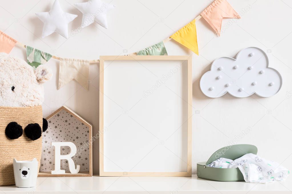 Stylish and modern scandinavian newborn baby interior with mock up photo or poster frame on the white shelf. Design toys, teddy bear and hanging cotton colorful flags, star and cloud. Template. Blank.