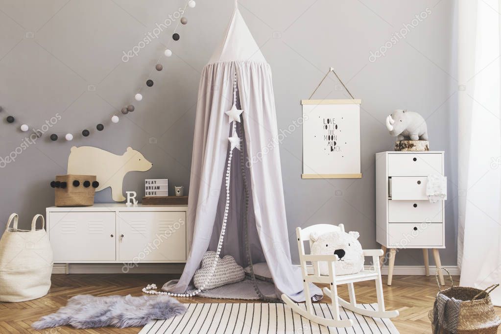 Stylish and bright scandinavian decor of newborn baby room with mock up poster, white design furnitures, natural toys, hanging grey canopy with wooden cradle, bookstand, accessories and teddy bears. 