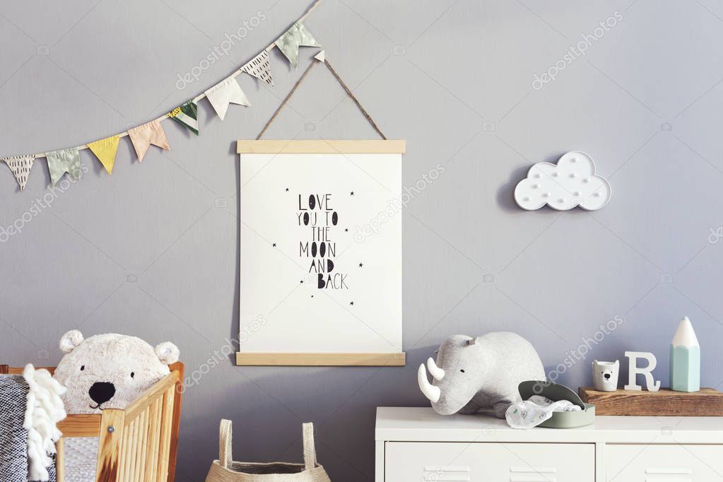 Modern and cute scandinavian decor of newborn baby room with mock up poster, natural toys, hanging decor flags and cloud, wooden cradle, basket for accessories and teddy bears. Grey walls. real photo.