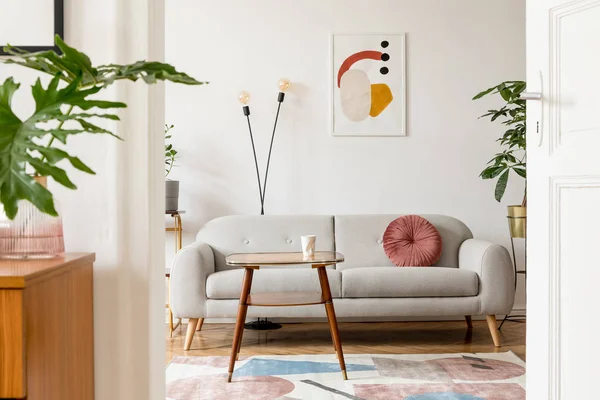 Stylish retro interior of living room with design commode, vinyl recorder, tropical leaf and mock up posters frames on the white walls. Cozy room with brown wooden parquet and plants.