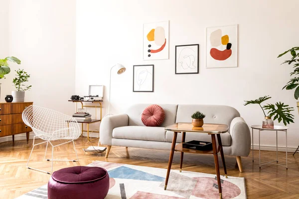 Gri kanepe, tasarım koltuk vintage sehpa, lamba ve şık süslemeleri ile oturma odası minimal retro iç tasarım. Parlak oda, duvarda brwon ahşap parke ve poster galerisi.