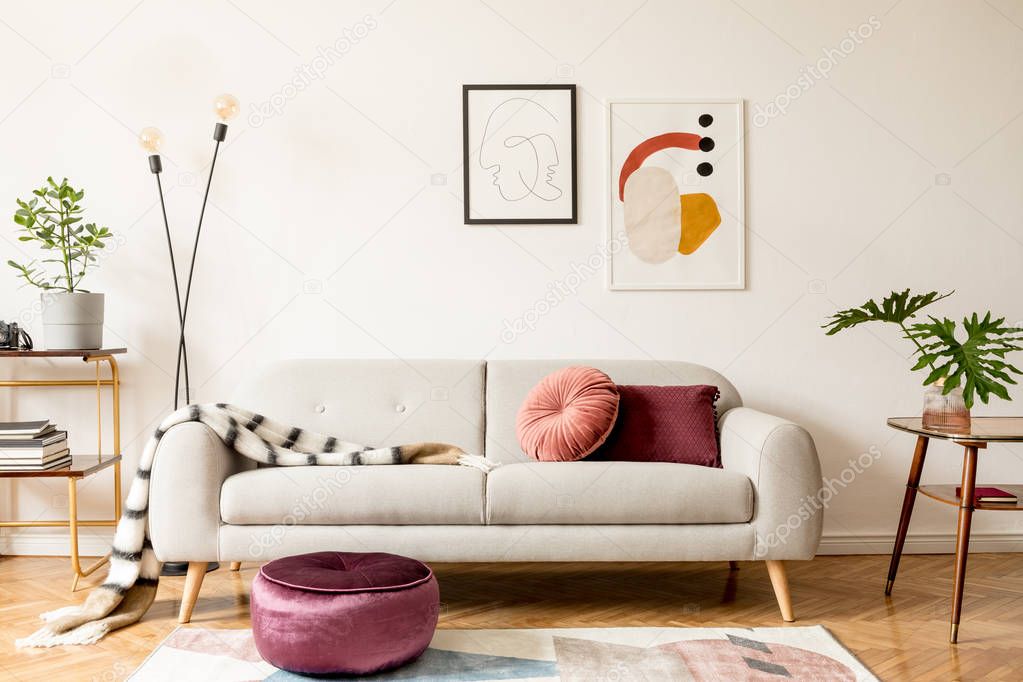 Stylish retro interior of sitting room with design sofa, gold bookstand, vintage table and mock up posters frames on the white walls. Interior design with brown wooden parquet, plants and leafs.