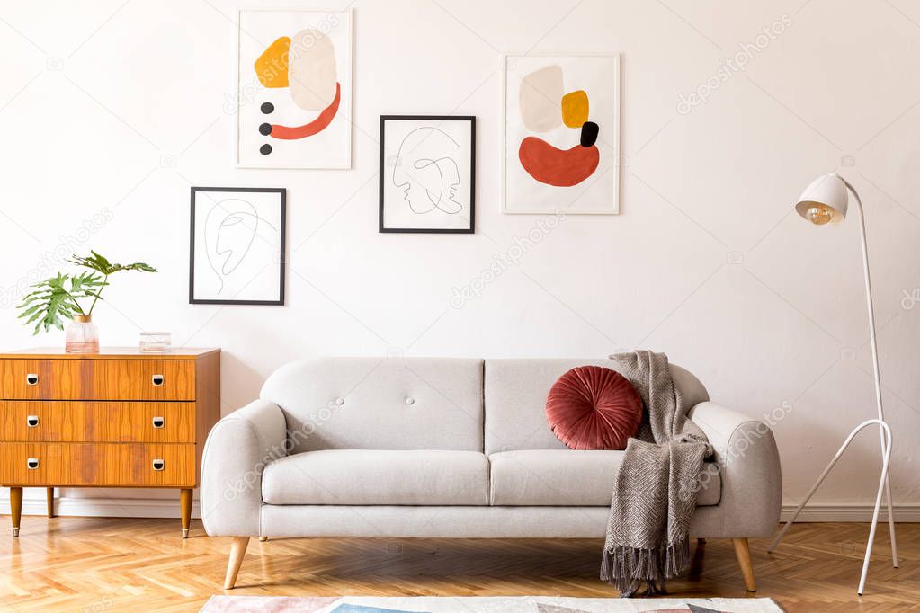 Stylish vintage decor in a spacious flat interior with design grey sofa, armchair, retro commode and posters on the wall. Brwon wooden parquet, stylish carpet and plants. Bright living room.