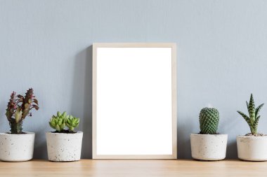 Güzel kaktüsler ve tasarım kapları succuletns ile kahverengi ahşap masada fotoğraf çerçevesi kadar sahte minimalist oda iç. Gri duvarlar. Sahte poster çerçevesinin şık konsepti. 