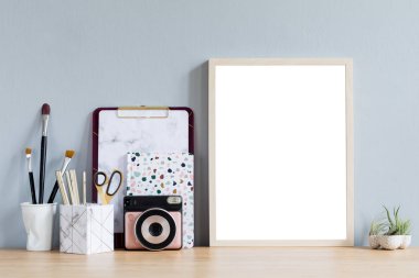 Ofis aksesuarları, anlık kamera, tasarım kaplar, defter ve notlar tillandsia ile kahverengi ahşap masa üzerinde sahte fotoğraf çerçevesi ile ev iç. Gri duvarlar. En az maket kavramı.