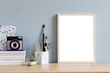 Ofis aksesuarları, anlık kamera, tasarım kaplar, kitap ve notlar tillandsia ile kahverengi ahşap masada sahte fotoğraf çerçevesi ile şık ev iç. Gri duvarlar. En az maket kavramı.