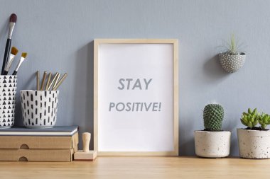 Aksesuarlar, kağıt kutuları, tasarım tencerekk, kalem fırçave damga ile kahverengi ahşap masa üzerinde fotoğraf çerçevesi kadar sahte İskandinav ofis iç. Gri duvarlar. En az maket kavramı.