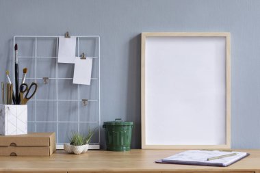 Ofis aksesuarları, kağıt kutusu, tasarım tencere, defter ve notlar hava tesisi ile kahverengi ahşap masa üzerinde sahte poster çerçevesi ile Home ofis iç. Gri duvarlar. En az maket kavramı.