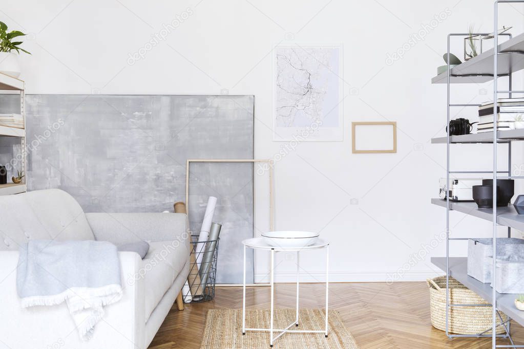 Modern nordic home interior with grey bookstand with accessories, design grey sofa, coffee table and modern furniture. Open space and living room for artist, freelancer, designer. Mockup poster frame