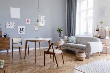 Tasarım İskandinav ev iç şık sandalyeler, aile masa ahşap komodin, gri kanepe, aksesuarlar ve posterler galeri duvar kadar sahte ile açık alan. Gri arka plan duvarları. Retro rahat ev dekorasyonu. 