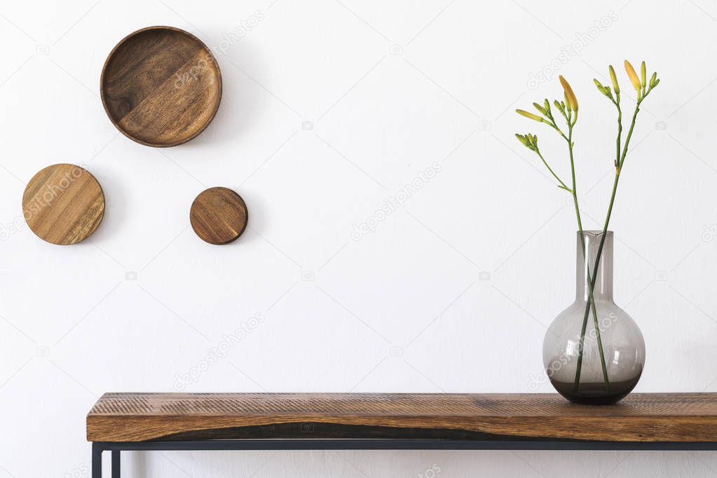 Stylish and modern scandinavian room interior with wooden console and rings on the wall, beautiful flowers in glassy vase. Design composition of home interior. White walls, copy space. Home decor.