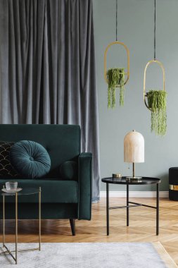 Yeşil kadife kanepe, tasarım sehpa, mermer masa lambası, asılı altın çiçekli ve zarif aksesuarları ile oturma odası şık ve lüks iç tasarım. Şablon. Modern ev dekorasyonu. 
