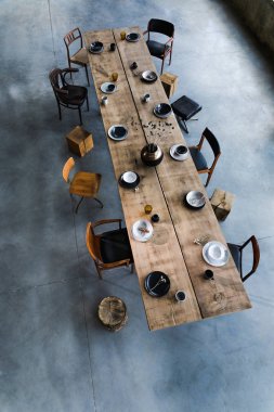 Yemek odasının içinde büyük ahşap masa, sandalyeler, tabaklar.