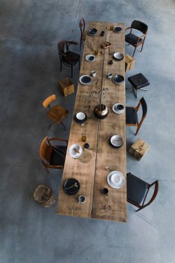 Yemek odasının içinde büyük ahşap masa, sandalyeler, tabaklar.