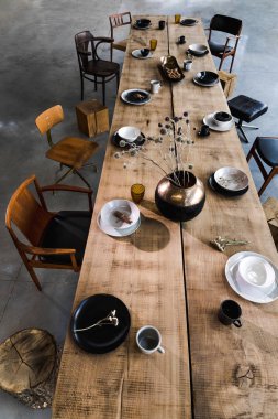 Yemek odasının içinde büyük ahşap masa, sandalyeler, tabaklar.