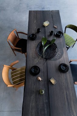 Yemek odasının içinde büyük ahşap masa, sandalyeler, tabaklar.