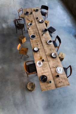 Yemek odasının içinde büyük ahşap masa, sandalyeler, tabaklar.