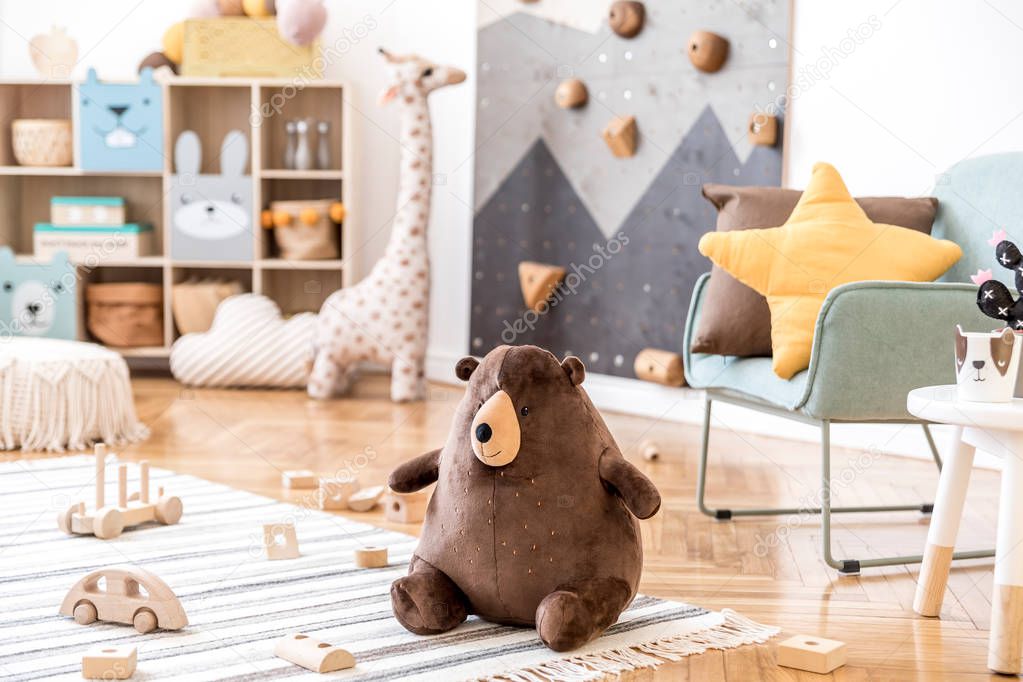 Modern scandinavian interior design of childroom with mint armchair, climbing wall for kids, design furnitures, soft toys, teddy bear and cute children's accessories. Stylish kidroom decor. Template.