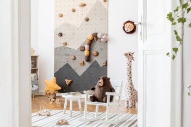 Çocuklar için modern tırmanma duvarları, mobilyalar, yumuşak oyuncaklar, koltukta oyuncak ayı ve sevimli çocuk aksesuarları olan şık bir iç tasarım. İskandinav oyun odası dekoru. Şablon.