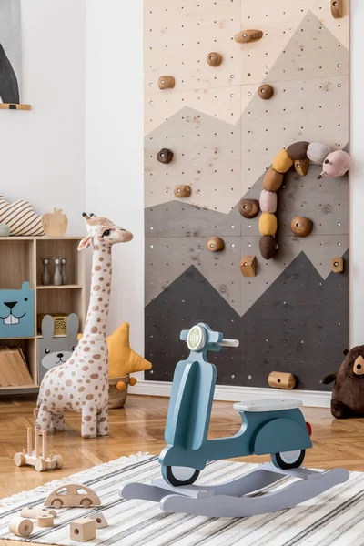 Scandinavian interior design of playroom with modern climbing wall for kids, design furnitures, kid\'s motor toy, soft toys, teddy bear and cute children\'s accessories. Stylish kidroom decor. Template.