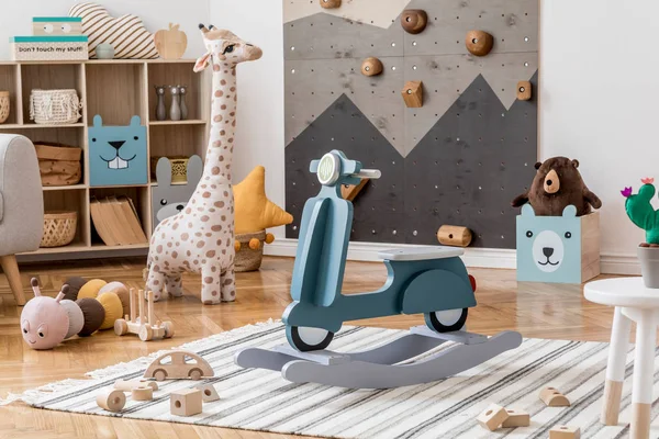 Scandinavian interior design of playroom with modern climbing wall for kids, design furnitures, kid's motor toy, soft toys, teddy bear and cute children's accessories. Stylish kidroom decor. Template.