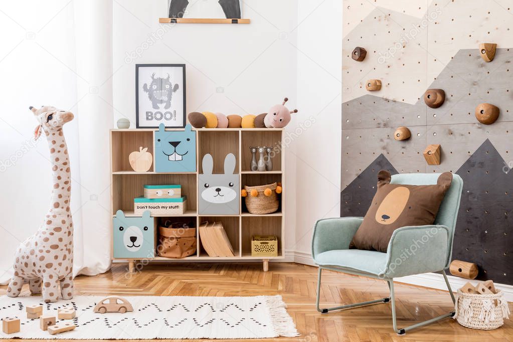 Scandinavian interior design of playroom with modern climbing wall for kids, design furnitures, mint armchair, soft toys, teddy bear and cute children's accessories. Mock up poster frame. Template.