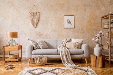 Tasarım gri kanepe, ahşap sehpa, raf, küp, halı, rattan kesesi, bitkiler, resim çerçevesi, masa lambası ve ev dekorunda zarif aksesuarlar ile oturma odasının iç kısımlarında şık bir skandi kompozisyonu..